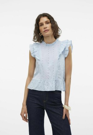 Lys blå, ermeløs topp med volanger på skuldrene, broderte detaljer og peplum-kant, parret med mørke denimbukser.