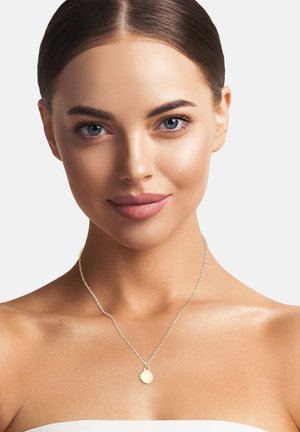 Goldenes Anhänger-Nelke an einer silbernen Kette mit einer runden, strukturierten Medaille. Glatte Haut und neutraler Hintergrund.