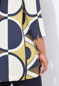 Tunika colorata con stampa geometrica che presenta grandi cerchi in navy, giallo e bianco. Realizzata in tessuto morbido con uno spacco laterale nella manica.