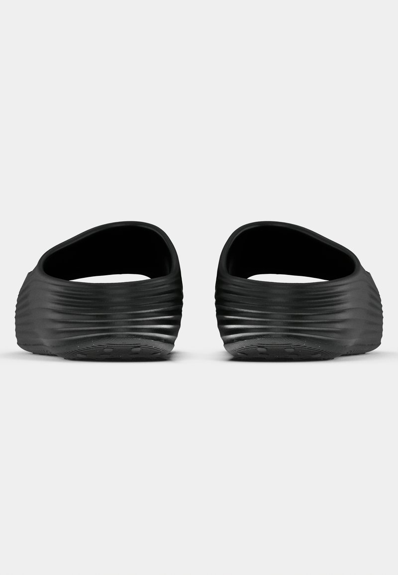 Zwarte instapschoenen met een ribbelstructuur, afgerond open ontwerp aan de bovenkant, platte zolen en een getextureerd grippatroon op de onderkant.