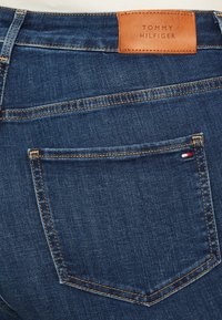 Dunkelblaue Denim-Jeans mit einem Lederlabel von TOMMY HILFIGER. Verfügt über orangefarbene Nähte und eine Gesäßtasche mit kleinen rot-, weiß- und blauem Details.