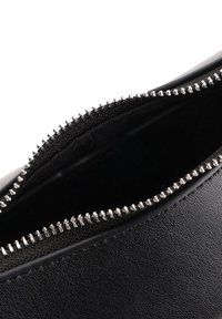 Intérieur d'un sac en cuir noir avec une fermeture éclair argentée et une doublure texturée. L'ouverture révèle un intérieur en tissu lisse et sombre.