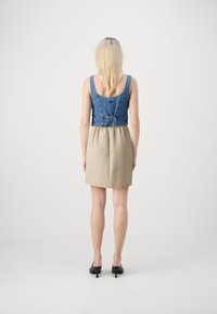 Haut en denim avec une taille ajustée, passant à une jupe beige. Dispose d'une boucle ajustable à l'arrière, avec une texture lisse et une forme en A.