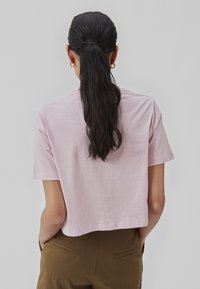 Kortærmet, cropped T-shirt i blød lyserød bomuld. Klassisk rund hals og glat tekstur. Båret med brune højtaljede bukser.