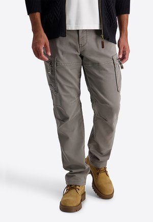 Man draagt grijze cargobroek met zijzakken en beige veterlaarzen, zichtbaar van taille tot voeten tegen een witte achtergrond.