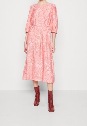 Różowa sukienka midi w kwiatowy wzór, z półdługimi bufiastymi rękawami, talią podkreśloną paskiem oraz lekko rozkloszowanym dołem, zestawiona z czerwonymi błyszczącymi botkami za kostkę.