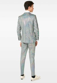 Traje de dos piezas para hombre con una tela holográfica brillante y un patrón cuadrado. Una camisa blanca y zapatillas casuales complementan el look.