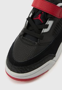 Sort og rød sneakers med sorte snørebånd, tekstureret læder og rød Jumpman-logo på tungen, med en hvid og rød sål.