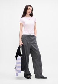 Hele roosa istega T-särk väikese logoga, kombineeritud hallide triibuliste laiadest pükstest. Must kott, mille sees on triibuline sveter.