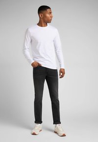 Vit långärmad skjorta, figurnära, kombinerad med mörka jeans. Skorna har en ljus bas med röda accenter. Enkelt, modernt design.