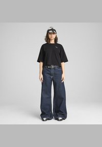 Čierne skrátené tričko s logom, široké tmavomodré denimové džínsy, opasok s cvočkami a čiapka s čierno-bielym vzorom. Neformálny mestský outfit.