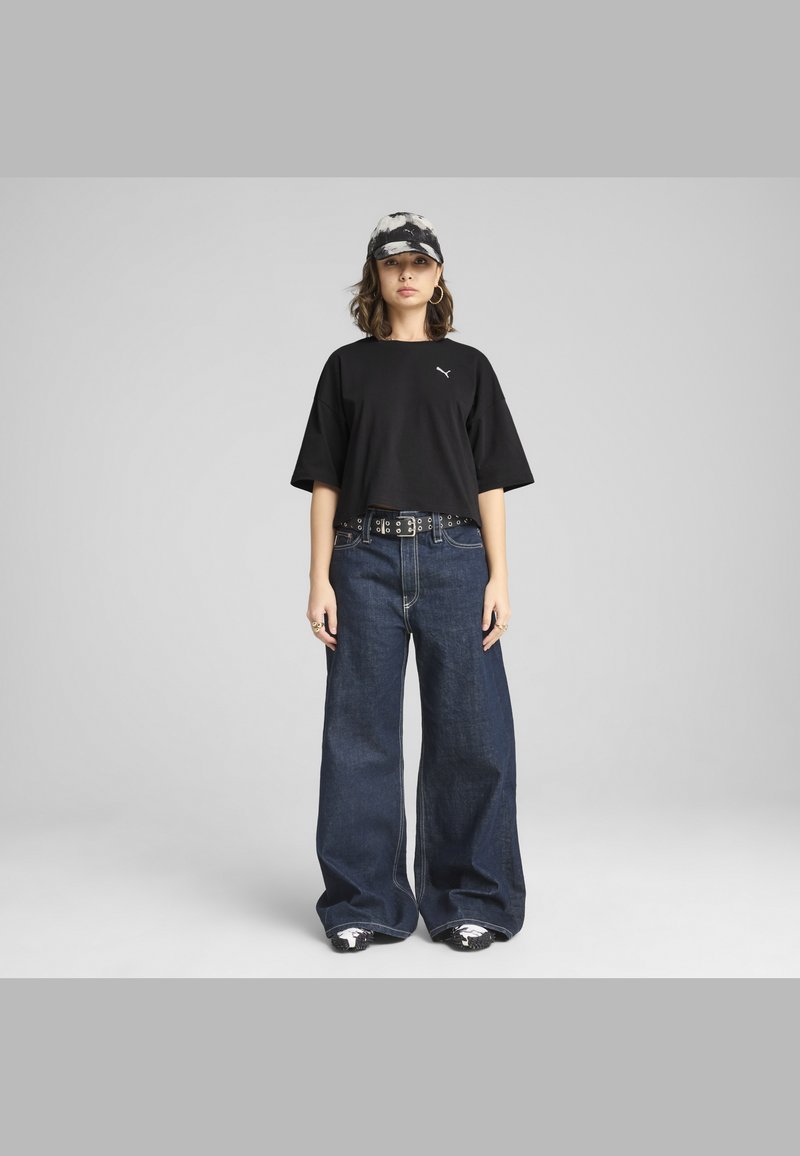 Čierne skrátené tričko s logom, široké tmavomodré denimové džínsy, opasok s cvočkami a čiapka s čierno-bielym vzorom. Neformálny mestský outfit.