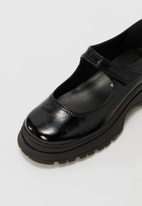 Μαύρα παπούτσια Mary Jane από πατενταρισμένο δέρμα με στρογγυλή μύτη, φαρδύ λουρί πάνω από το δάκτυλο και χοντρή καουτσούκ σόλα.