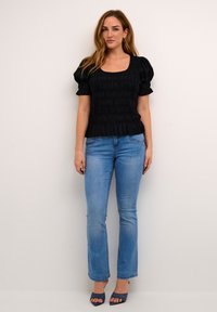 Sort smocket bluse med korte puffærmer, parret med lyseblå lige ben jeans og navy åben tå hæle. Simpelt, tekstureret design.