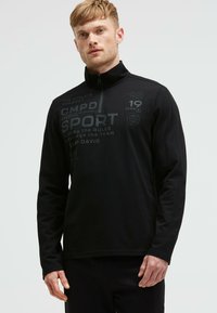 Schwarzes Sportoberteil mit langen Ärmeln und hohem Kragen, ausgestattet mit einem Teilreißverschluss und bedrucktem Text in verschiedenen Grautönen für Designdetails.