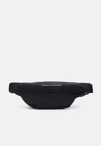 Marsupio in nylon nero a forma curvata, dotato di una tasca frontale con zip e logo bianco "TOMMY HILFIGER". Tessuto testurizzato per una maggiore durata.