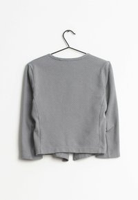 Långärmad grå topp med ett strukturerat mönster av små vita prickar, med en rund halsringning och en böjd nederkant bak.}}