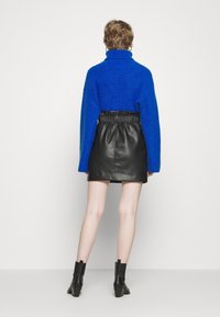 Maglione blu chunky con colletto alto abbinato a una mini gonna in pelle nera. Stivali neri alla caviglia completano l'outfit.