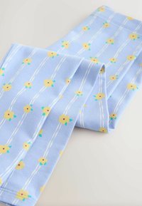 Světlé modré legíny s květinovým vzorem, žlutými květy a zelenými detaily, texturovaná látka a bílé svislé pruhy.