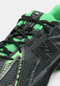 Chaussure de sport gris foncé avec des accents verts vifs. Caractéristiques d'un tissu texturé, de lacets noirs et d'un logo distinct. Design élégant et moderne.