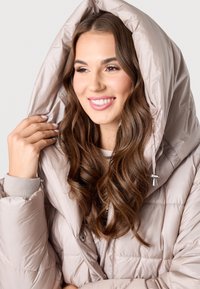 Helle beige Steppjacke mit großem, kapuzenartigem Kragen. Verfügt über ein gesteppte Design, silberne Beschläge und elastische Bündchen. Weiche Textur.