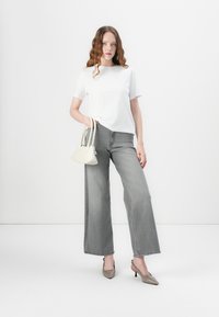 Hvit t-skjorte med korte ermer, grå vidjeans, beige håndveske med to håndtak, og grå høyhælte sko. Glatte teksturer og nøytrale farger.