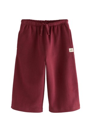 Shorts bordeaux longueur genou avec taille élastique, cordon de serrage, poches latérales et petite écusson crème avec motif arc-en-ciel sur la jambe gauche.