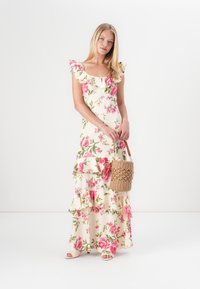 Blommig maxiklänning med volangärmar, med en krämfärgad botten och rosa blommönster. Matchas med en vävd stråväska och sandaler.