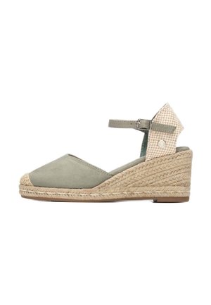 Cuña de esparto de ante verde con suela de yute tejida, correa en el tobillo y un detalle de tela a cuadros en el talón. Diseño con punta baja.
