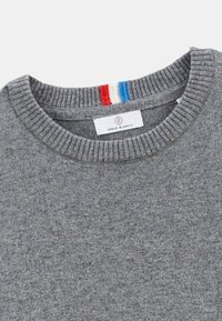 Un pull gris avec un col côtelé présentant une bande rouge, blanche et bleue. L'étiquette indique "SERGE BLANCO." Texture douce et design décontracté.