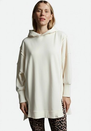 Kapuzenpullover in Off-White, mit lockerer Passform, weichem Stoff, gerippten Bündchen und seitlichen Schlitzen; kombiniert mit schwarzen Leggings im Leopardenmuster.