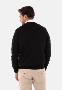 Maglione nero a maglia con maniche lunghe, polsi e orlo a coste. Design semplice senza motivi, indossato su pantaloni chiari.