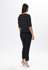 Pull noir avec des rayures blanches horizontales, manches courtes et col rond. Associé à un pantalon noir ajusté et des sandales à talons hauts argentées.