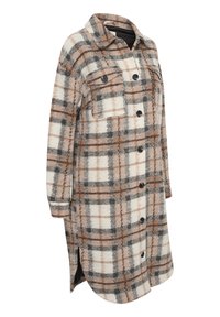 Camisa chaqueta de franela a cuadros en crema, marrón y gris. Cuenta con un cierre frontal de botones, dos bolsillos en el pecho y aberturas laterales en el dobladillo.