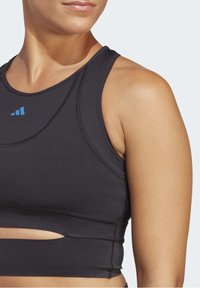 Černý sportovní crop top s přiléhavým designem, který má modrou logo, texturovanou látku a detail s bočními výřezy.