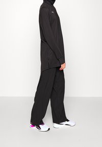 Svart långärmad topp med sidöppningar, kombinerad med lösa svarta byxor och vita sneakers med rosa detaljer och svarta inslag.