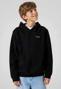 Zwarte hoodie met een buidelzak en geribbelde cuffs, met het logo "T.W.S.N." in het wit op de linker borst. Draagt met lichtblauwe jeans.