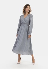 Blauwe maxi-jurk met bloemenprint, een diepe V-halslijn, lange mouwen en een elastische taille. Heeft een vloeiende rok en geplooide details bij de polsen.