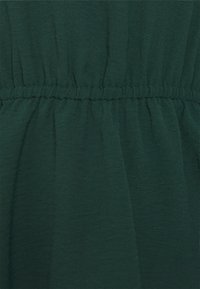 Tissu vert texturé avec des détails froncés à la taille, présentant une apparence douce et légère ainsi que des variations subtiles de teinte.