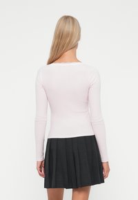 Top a maniche lunghe rosa chiaro con scollatura bordata in pizzo, abbinato a una gonna plissettata nera. Il tessuto appare morbido e aderente.