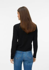 Pull noir à manches longues avec un col rond, design ajusté et texture douce, associé à un jean bleu taille haute.