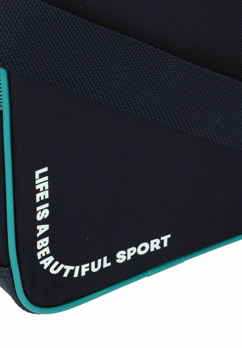 Pochette en tissu bleu marine avec accents turquoise. Porte le texte « LA VIE EST UN SPORT MAGNIFIQUE » en blanc. Le texte est positionné le long du bord du design.