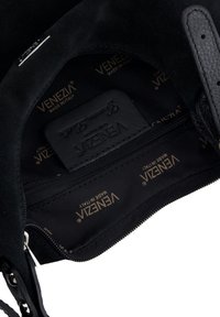 Sort ruskind taskeindvendigt med en lynlåslomme, læderetiket præget med "Venezia" og et satinforet med guldfarvet branding.