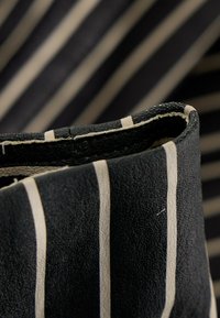Gros plan d'un tissu noir plié avec des rayures verticales blanches et des détails de couture visibles.