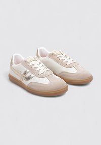 Zapatillas de ante beige y cuero blanco con detalles metálicos dorados, puntera redondeada, cordones blancos y suela de goma color caramelo.