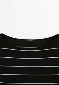 Czarna dzianinowa bluzka w białe poziome paski z okrągłym dekoltem, z widoczną metką odzieżową z tyłu wewnątrz kołnierza.