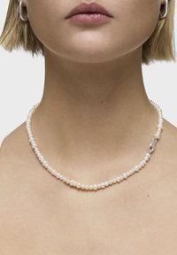 Collana di perle con piccole perle bianche di forma irregolare, caratterizzata da una chiusura in argento. Superficie liscia con una lucentezza sottile.