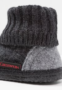 Wool slipper with a knitted black upper and gray felt body. Features textured material, a black sole, and a red brand label on the side.