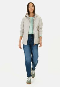 Lichtgrijze gewatteerde jas met capuchon, gecombineerd met een groen en wit gestreept shirt en blauwe denim jeans. Voorzien van casual groene sneakers.