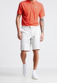 Rödrandig polo med Nike-logga, kombinerad med vita shorts. Vita sneakers fulländar outfiten. Korta ärmar och skräddarsydd passform.